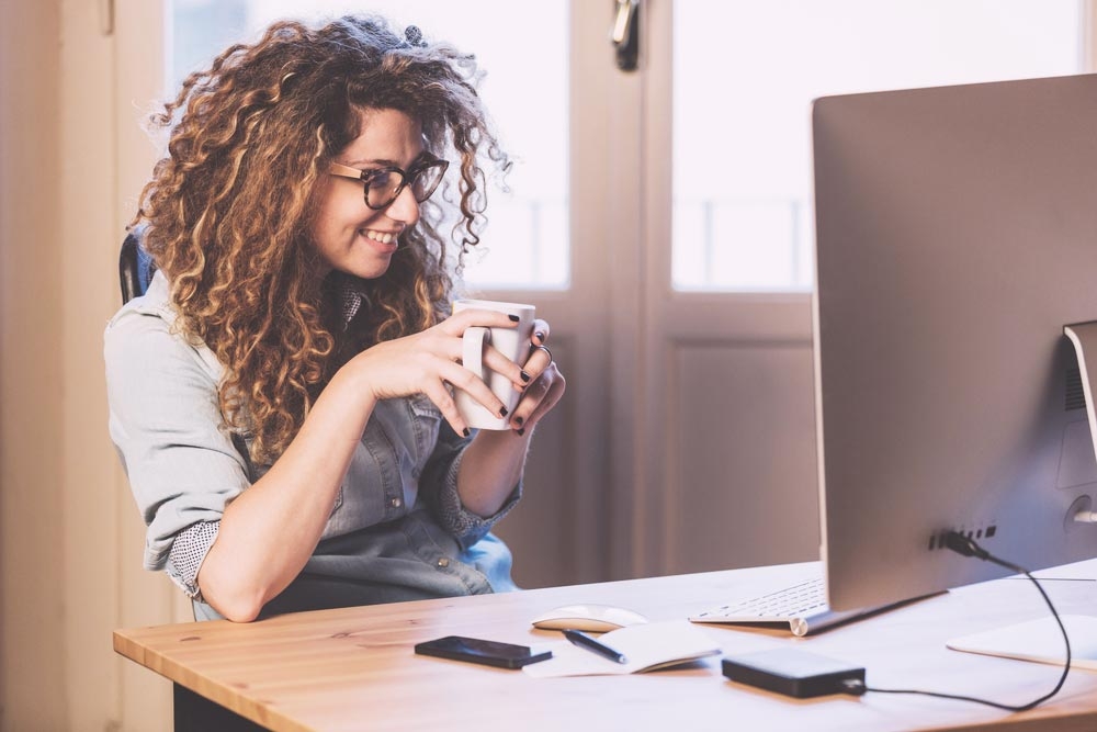 Girl drinking coffee and looking at a monitor