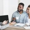 A couple sits with coffee mugs and speaks with a mortgage broker or financial advisor