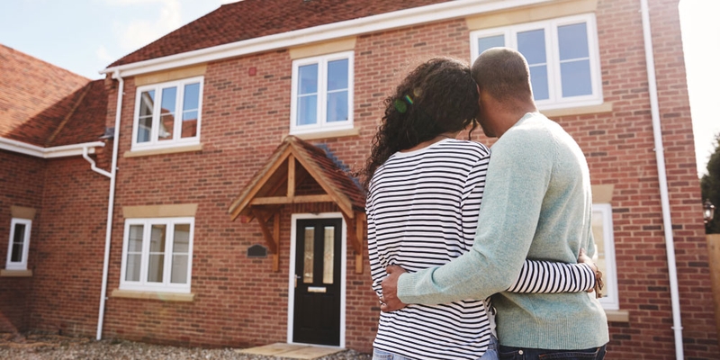 A man and woman embrace in front of their brick house