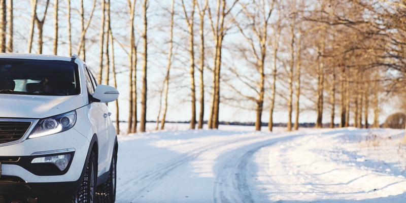 A white SUV drives along a snowy road