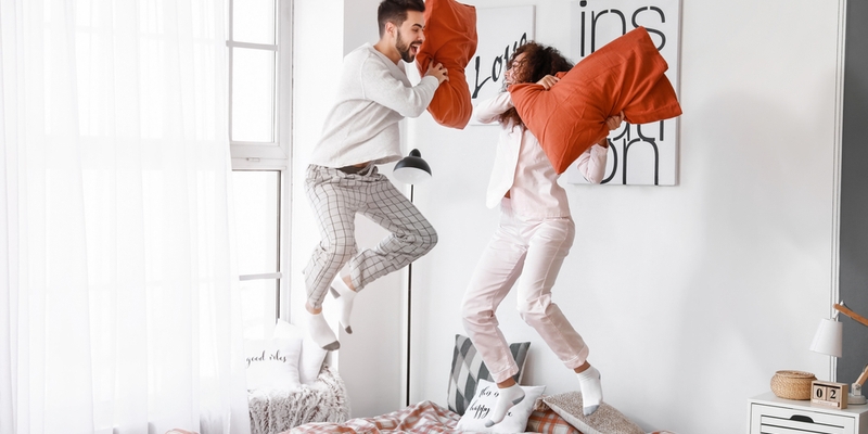 Happy young couple fighting on pillows in bedroom.jpg