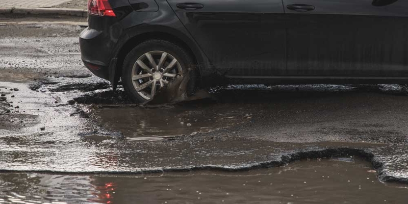 A black car drives over a pothole in the road