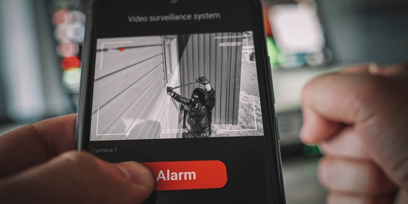 Protection of private residential building with help of an external video surveillance system. an application on smartphone screen. CCTV view of burglar breaking into home through window with crowbar.