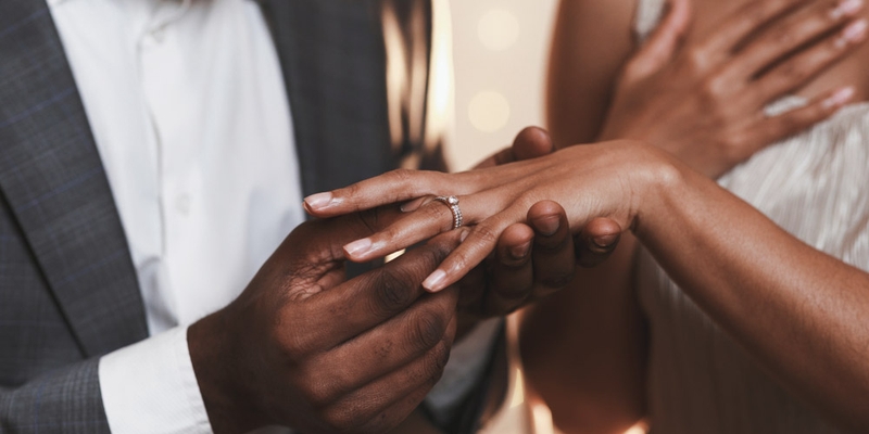 A man holds a woman's hand with an engagement ring on it