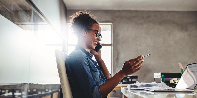 A trendy young woman works in a modern coworking space and chats happily on her phone
