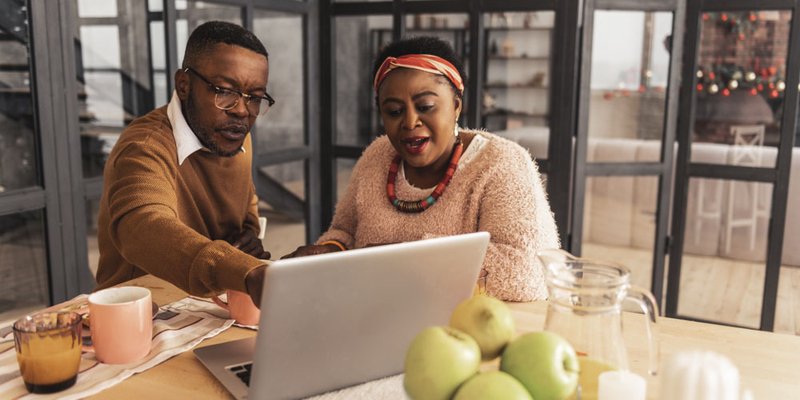 African American couple sitting at modern kitchen looking on their laptop