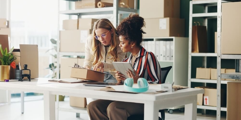 Women, tablet and teamwork for office logistics, package and e commerce checklist with stock of online shop. Small business people or seller with digital tech, box and clipboard for website order