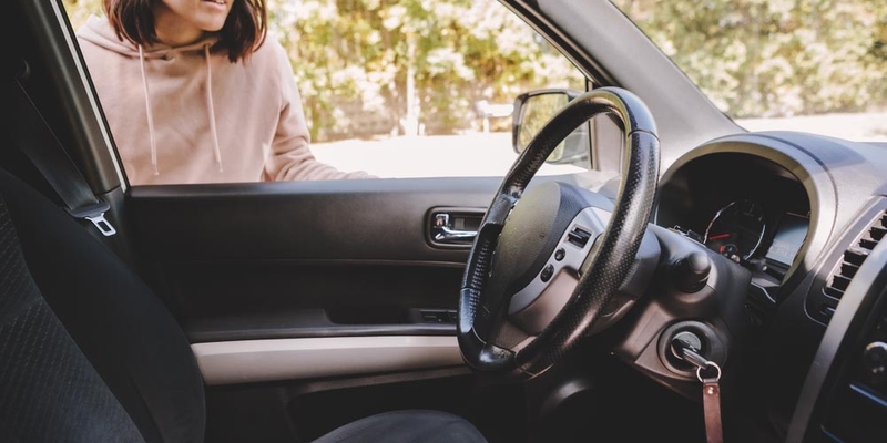 A woman looks in the window of her car to see her keys locked inside