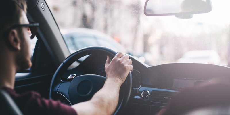 A man sits behind the driver's seat of his vehicle on a sunny day