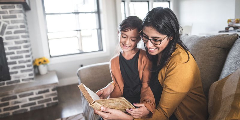 Mom reads to her daughter on their couch in modern home