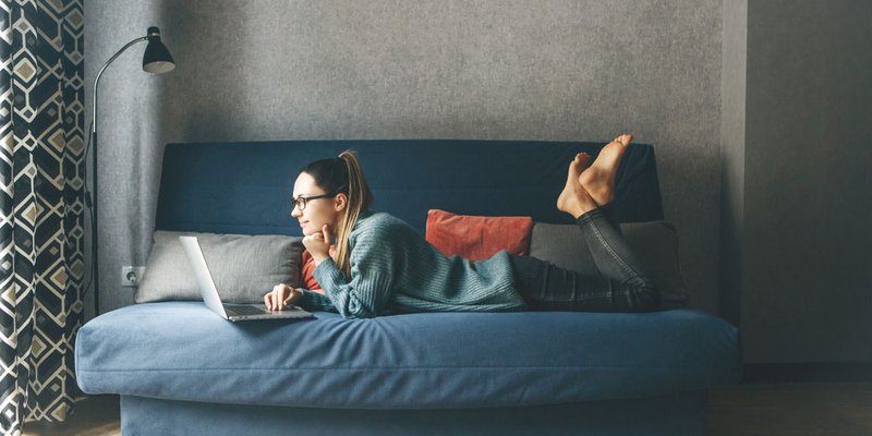 Woman laying on her couch in small urban apartment on her laptop