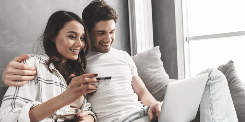 A man and a woman lounge on a couch and online shop together