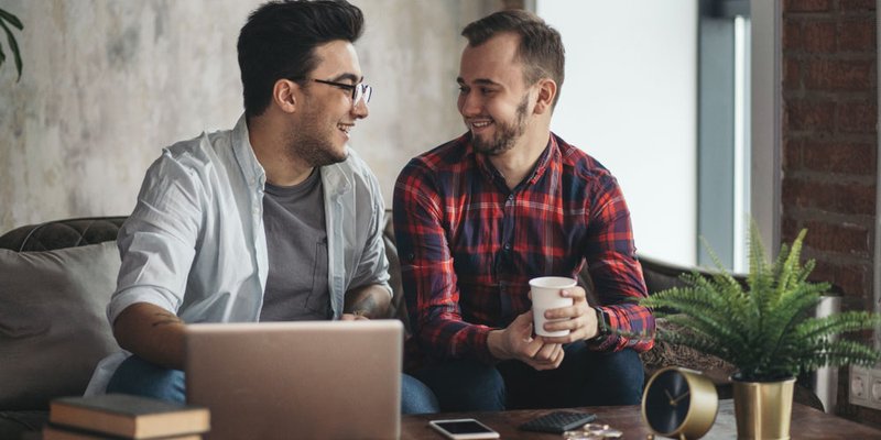 Two men sit talking to one another and review what's on the laptop