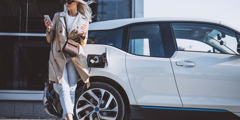 A woman leans against her electric vehicle while it charges