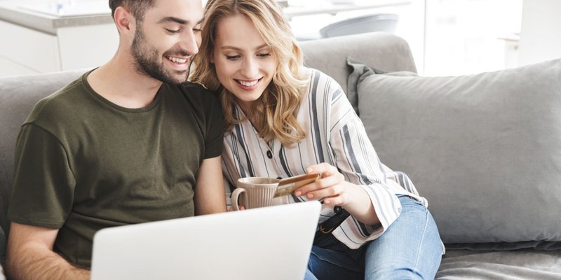 A young couple shop online using their credit card while sitting on the couch