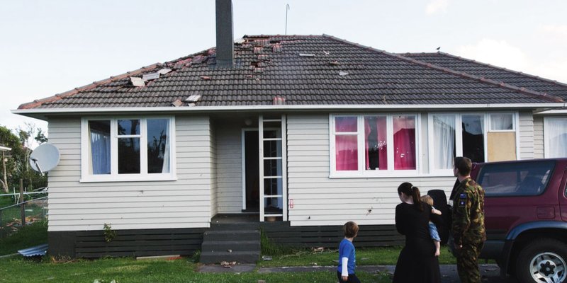 A wind damaged home with missing shingles and debris on the lawn